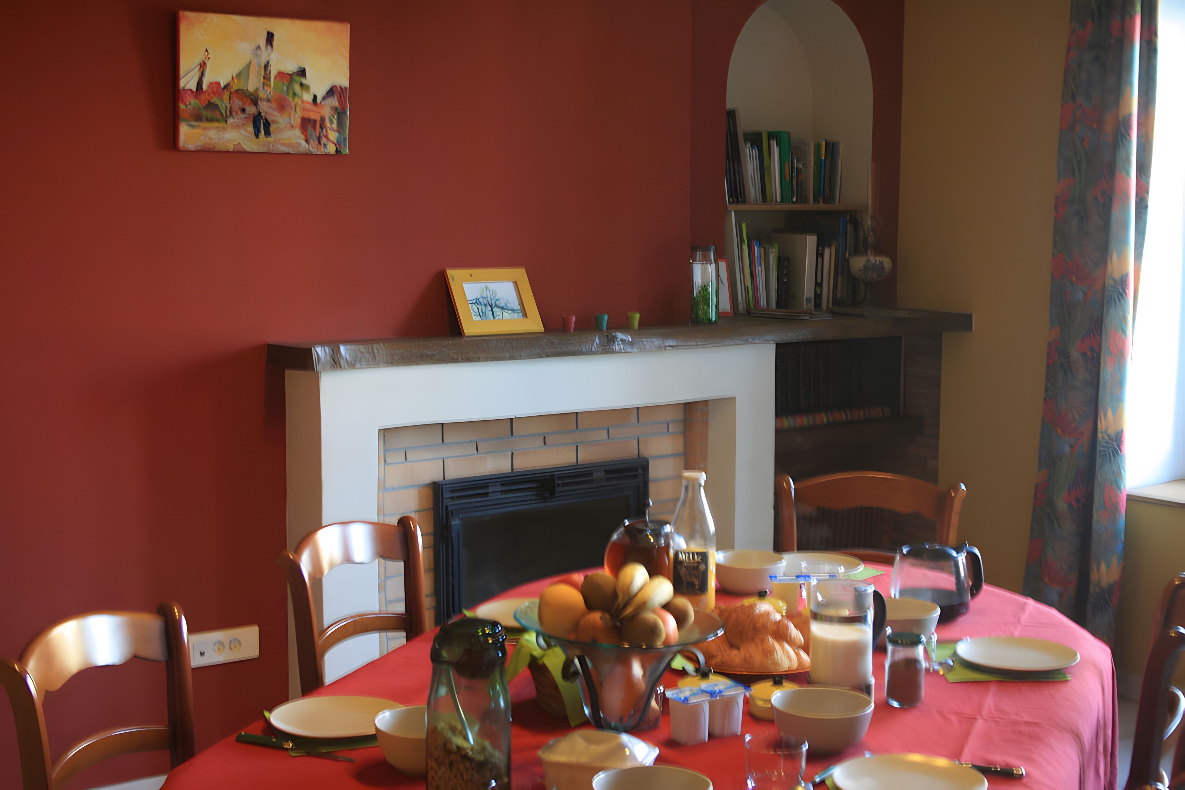 Une salle à manger avec une table rouge mise pour le petit-déjeuner, une cheminée et une bibliothèque.