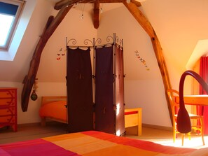 A room with a sloped ceiling, a bed with a colorful quilt, a wooden chair, a small table, and a wardrobe with a metal frame. - Bed and Breakfast 'Chambres Framboise' with Shared Garden and Wi-Fi (Cheillé)