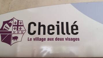 A sign with the word 'Cheillé' and a shield emblem with a bird, fleur-de-lis, and a pig.