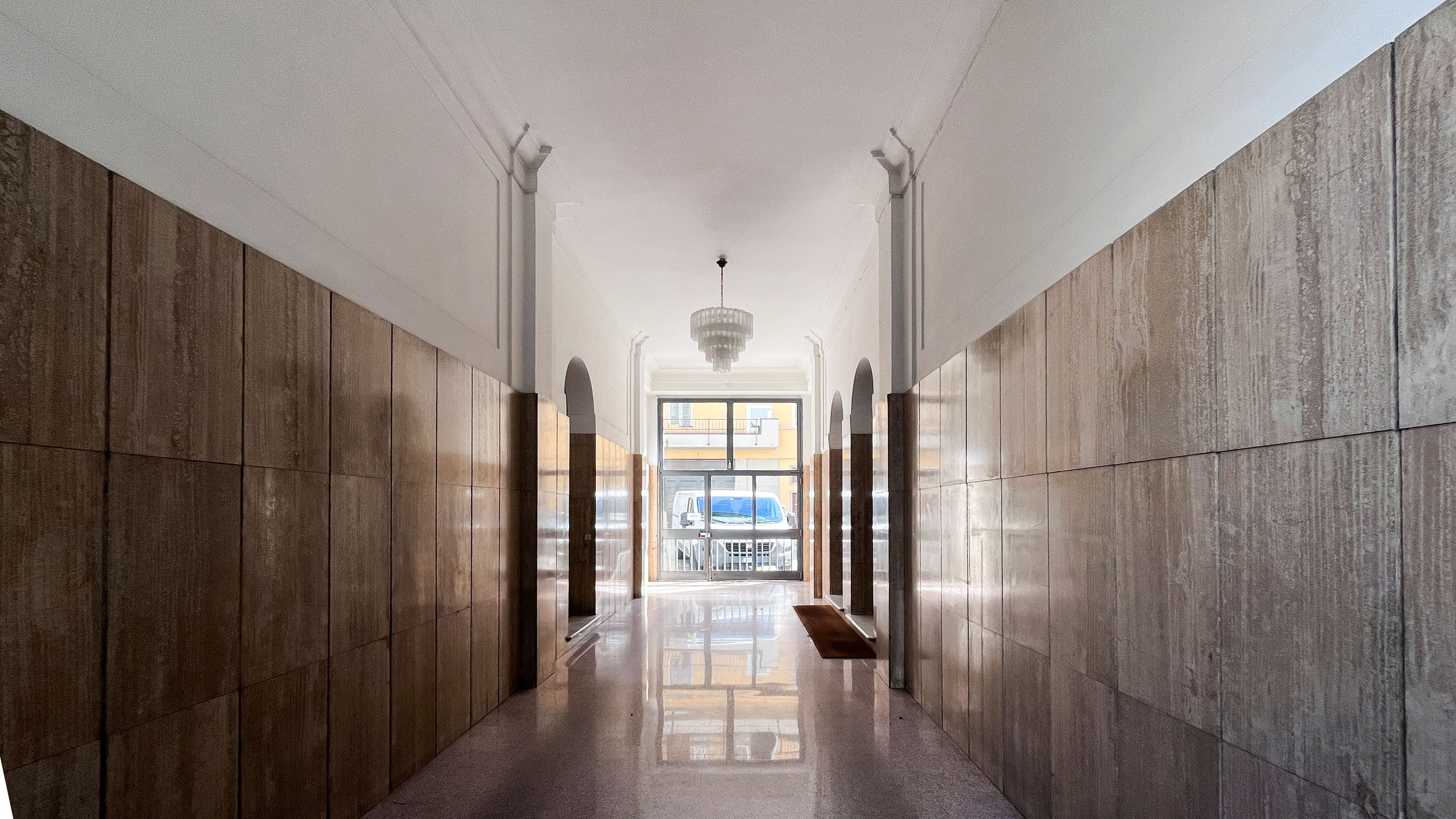 A hallway with a polished floor, tall columns, and a large window at the end.