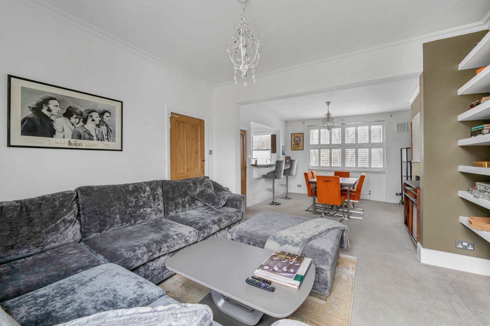 A modern living room with a grey sofa, a coffee table, and a dining area with orange chairs.