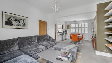 A modern living room with a grey sofa, a coffee table, and a dining area with orange chairs.