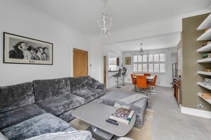 Een moderne woonkamer met een grijze bank, een salontafel en een eethoek met oranje stoelen.