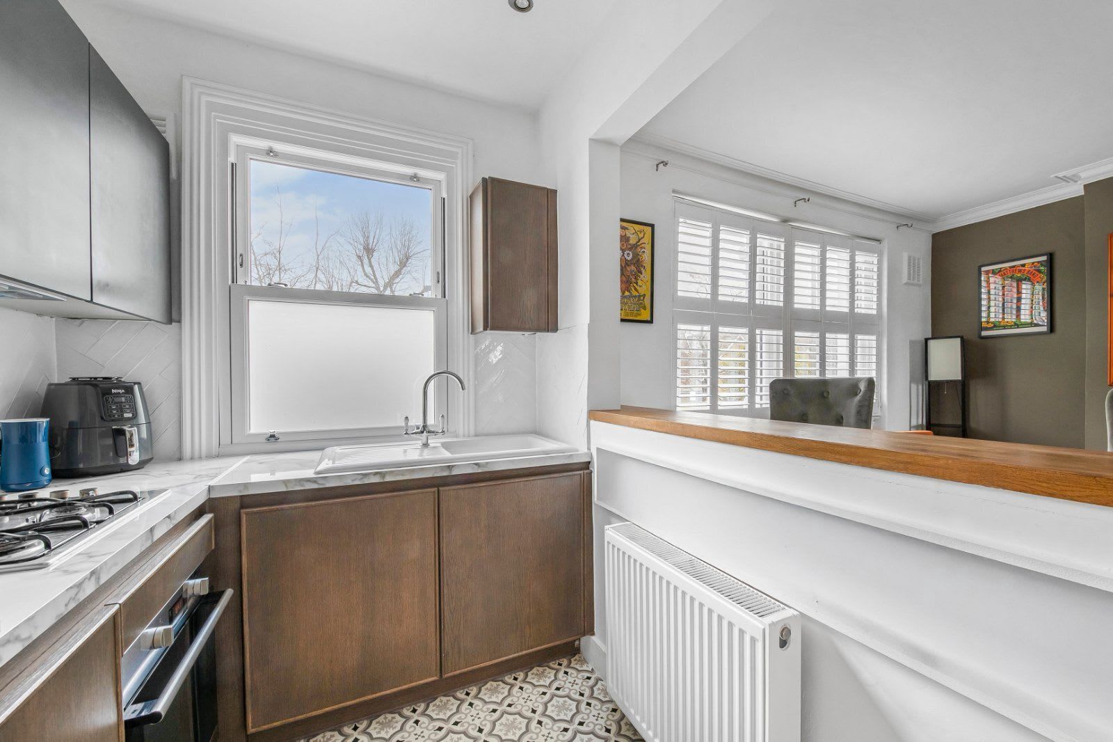 A compact kitchen with a built-in stove, a sink, and a window with blinds.
