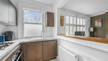 A compact kitchen with a built-in stove, a sink, and a window with blinds.