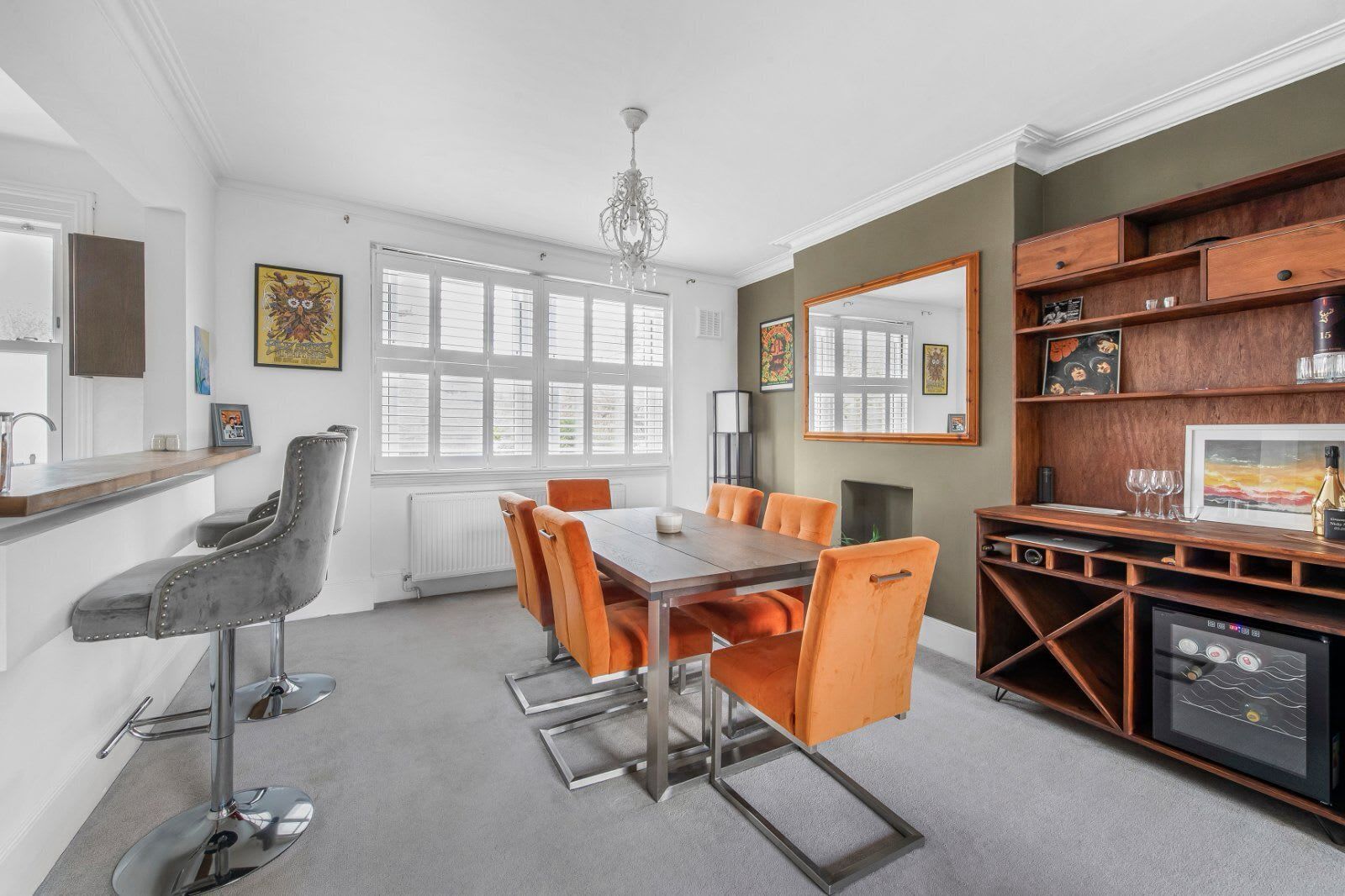 Ein moderner Essbereich mit einem Holztisch und orangefarbenen Stühlen, ein Küchenbereich mit integriertem Geschirrspüler und ein großer Spiegel an der Wand.