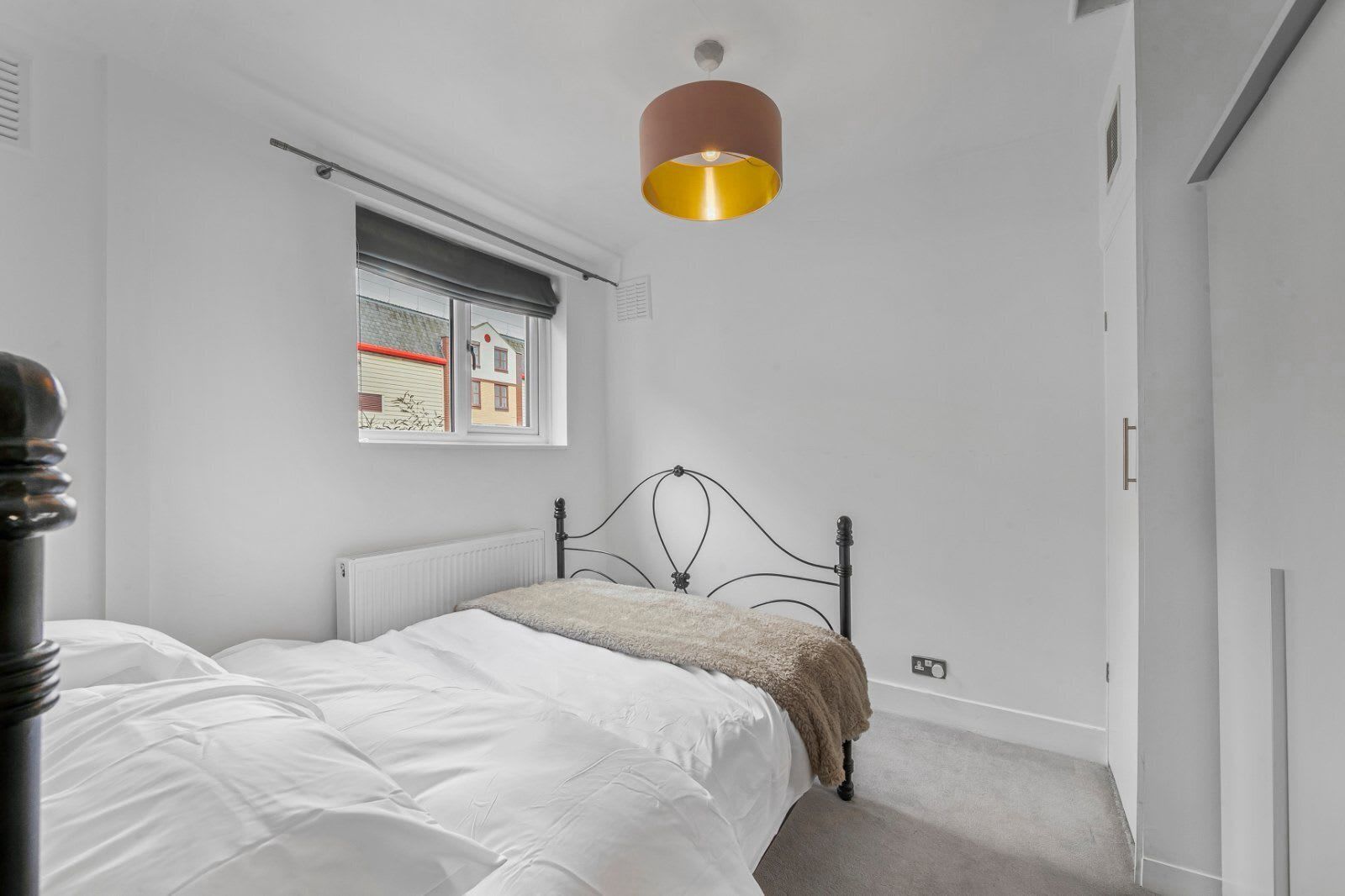 A bedroom with a bed, a window with a view, a radiator, and a pendant light.