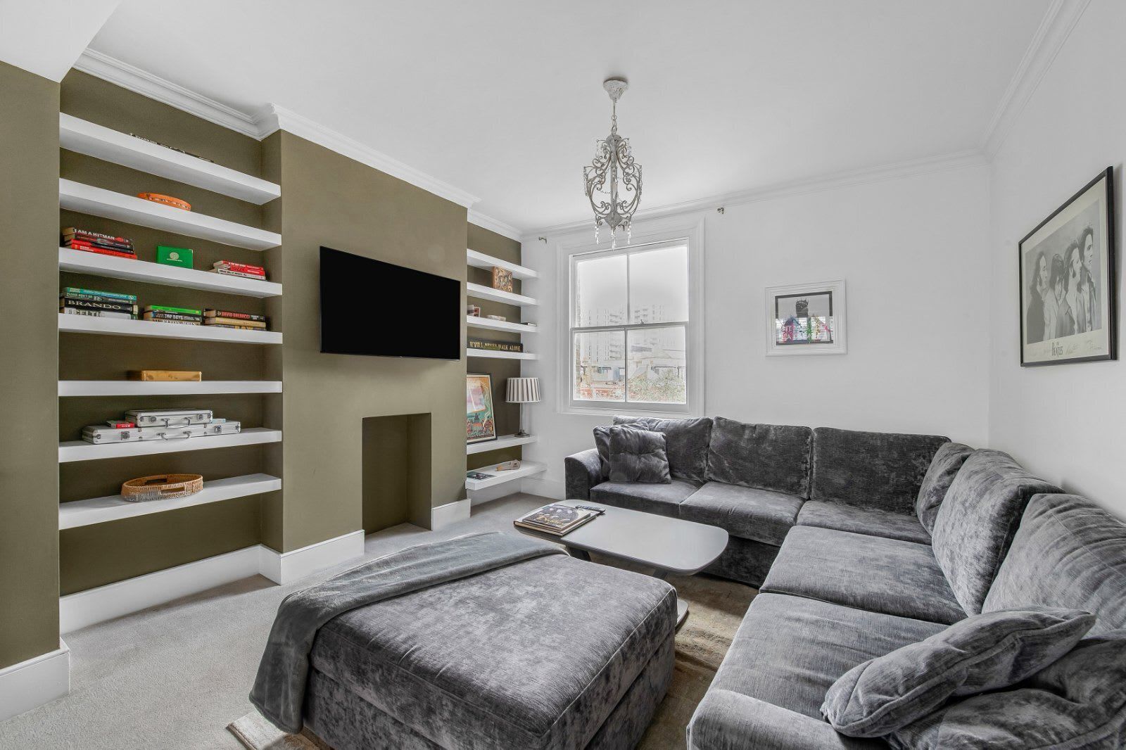 A living room with a sectional sofa, a flat-screen TV, and built-in shelving with books and decorative items.
