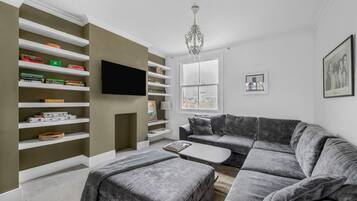 A living room with a sectional sofa, a flat-screen TV, and built-in shelving with books and decorative items.