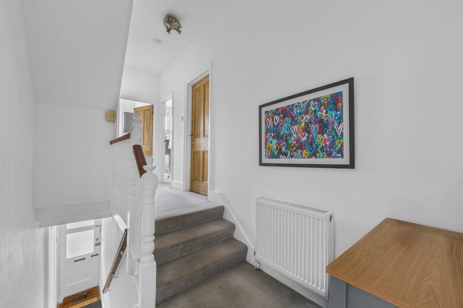 Een trap met een witte leuning, een radiator en een lijst met abstracte kunst aan de muur.