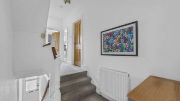 Een trap met een witte leuning, een radiator en een lijst met abstracte kunst aan de muur.