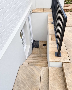 A staircase with beige tiles leading to a landing, a black metal railing on the right, and a white wall with a window on the left. - Central 1-bed apartment moments from Guildford train station (guildford)