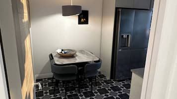 Ett kompakt kök med ett matbord, stolar, en hängande lampa och ett kylskåp.
