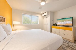 Une chambre d’hôtel équipée d’un lit, d’une télévision, d’un ventilateur de plafond et d’une fenêtre avec des stores.