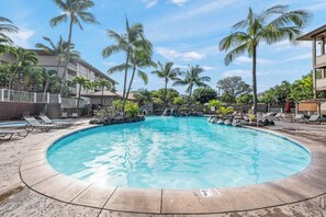 A circular swimming pool with lounge chairs and palm trees, surrounded by a building with a balcony. - 2BR Apt near Kam 1 Beach, Pool, Hot Tub, BBQ (Kihei)