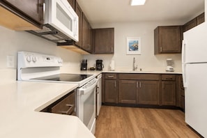 A kitchen with a built-in oven, microwave, and dishwasher, wooden cabinets, and a white countertop. - 2BR Apt near Kam 1 Beach, Pool, Hot Tub, BBQ (Kihei)