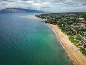 Eine Luftaufnahme einer Küstenlandschaft mit Strand, Gebäuden und einem Berg im Hintergrund.