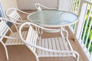 A white metal table and chairs on a balcony with a glass top, surrounded by white railings and greenery. - 3x3BR ¼ mi to Kam 1 Beach, Pool, Hot Tub, Gym, BBQ (Kihei)