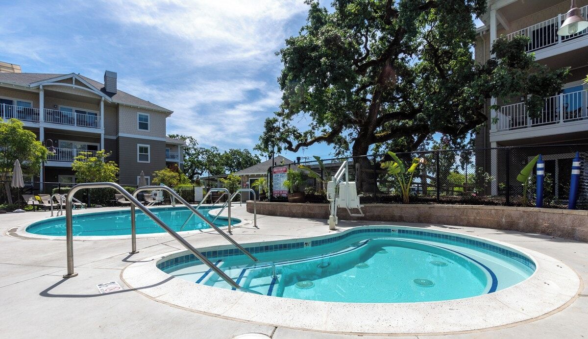 A residential building with a swimming pool, outdoor furniture, and a large tree.