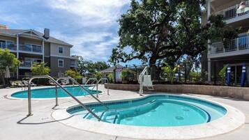 A residential building with a swimming pool, outdoor furniture, and a large tree.