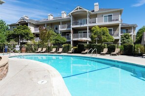 A swimming pool with lounge chairs, a multi-story building with balconies, and a clear sky. - Professionally managed 3BR Condo, Pool, Fireplace, BBQ (Windsor)