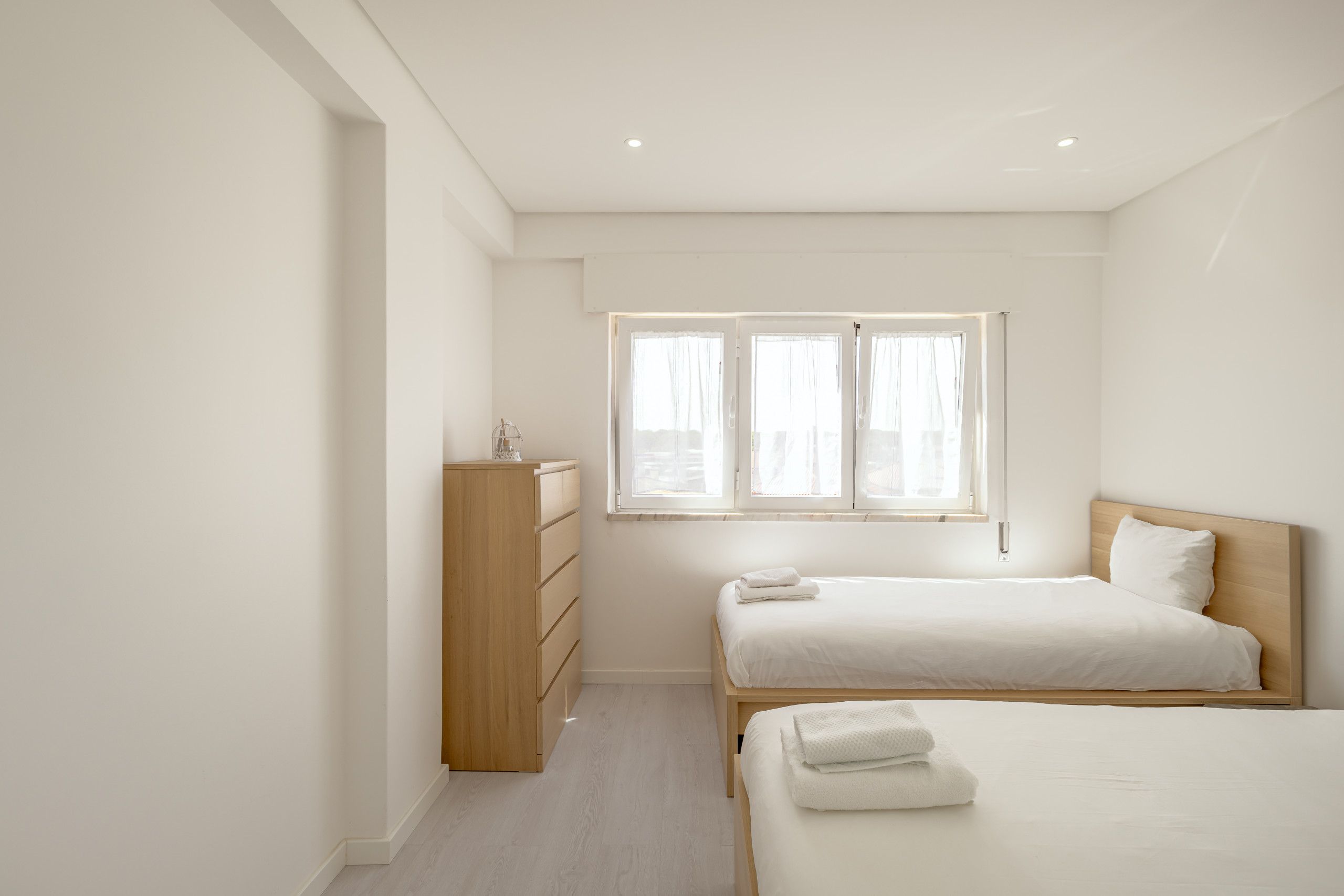 Un dormitorio minimalista con dos camas, un armario de madera y una ventana con cortinas.