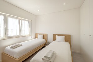 Une chambre d’hôtel avec deux lits simples, une grande fenêtre et un mur blanc uni.