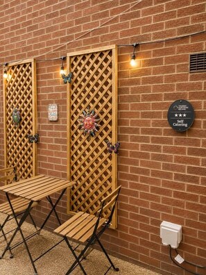 A brick wall with two wooden lattice doors, a table with chairs, and a sign indicating self-catering facilities. - The Cosy Claddagh – Spacious 3-Bedroom Belfast Home (Belfast)