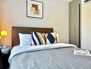 Ein ordentlich bezogenes Bett mit einer grauen, strukturierten Bettdecke, einem braunen Kopfteil und mehreren Kissen in verschiedenen Farben.