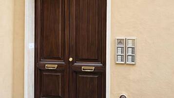 Una doble puerta de madera con manijas de latón y un umbral de bronce, ubicada en una pared beige con un letrero azul con la letra 'A'.