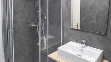 Un baño moderno con ducha de vidrio, lavamanos blanco y espejo sobre él.