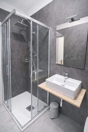 Un baño moderno con ducha de vidrio, lavamanos blanco y espejo sobre él.