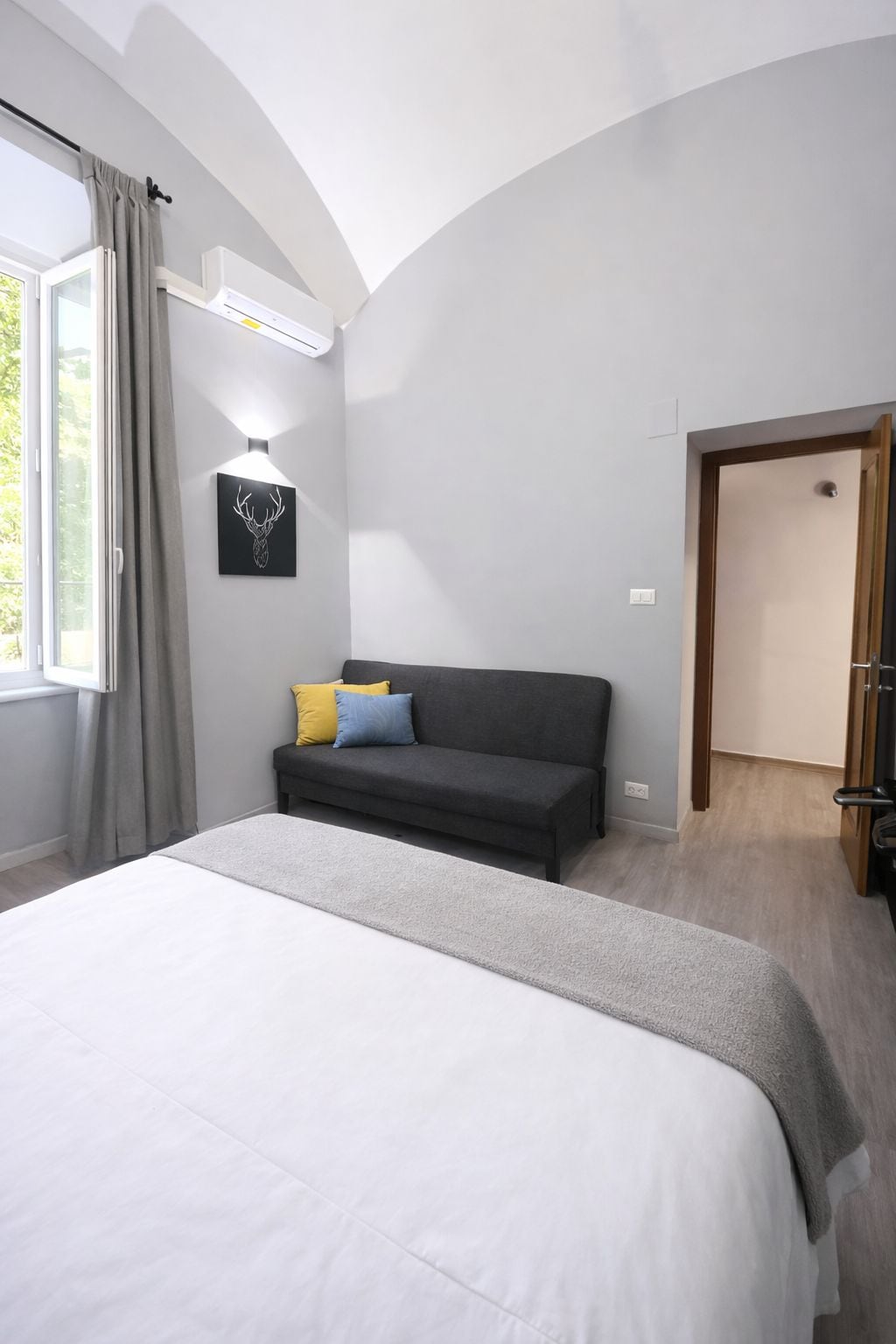Un dormitorio con una cama, un sofá oscuro, una lámpara en la pared y una puerta.