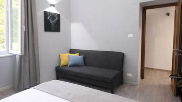 Un dormitorio con una cama, un sofá oscuro, una lámpara en la pared y una puerta.