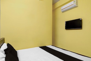 Habitación de hotel con cama, televisor de pantalla plana en la pared y equipo de aire acondicionado sobre el televisor.