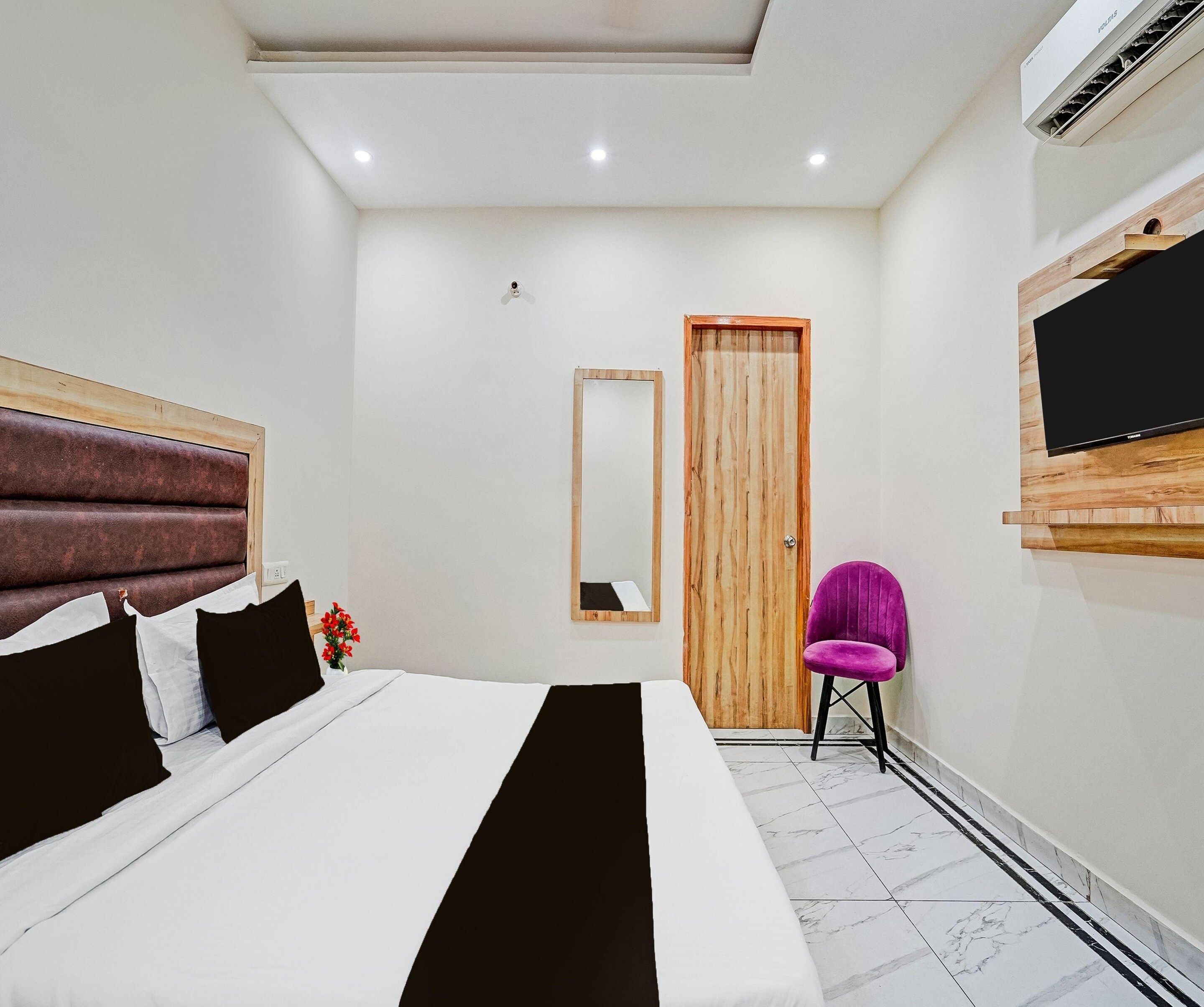 A modern hotel room with a large bed, a wooden door, a mirror, and a flat-screen TV mounted on the wall.
