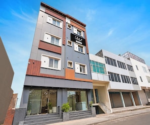A multi-story building with a modern architectural design, featuring a mix of wood and metal paneling, large windows, and a visible entrance with steps leading to the ground floor.