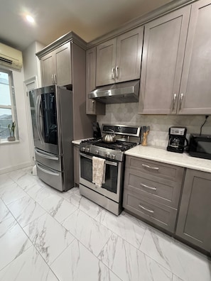 A kitchen with stainless steel appliances, marble flooring, and grey cabinetry.
