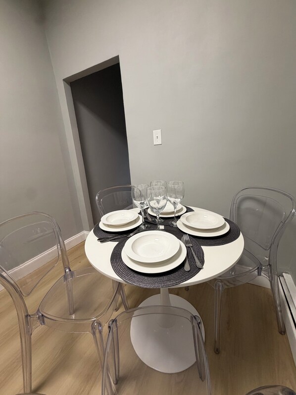 A dining table set with white plates, black placemats, and clear glassware, surrounded by transparent chairs.