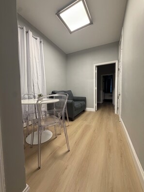 A modern living space with a dining area, a sofa, and a hallway leading to another room.