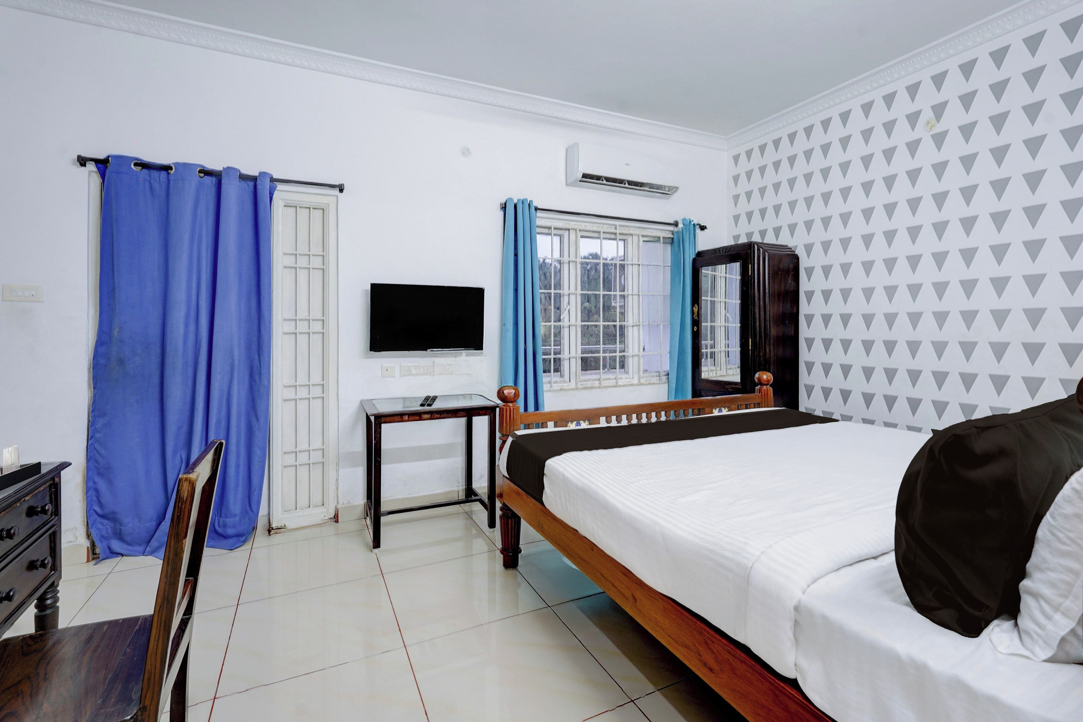 A hotel room with a bed, a desk, a chair, a TV, and a window with curtains.