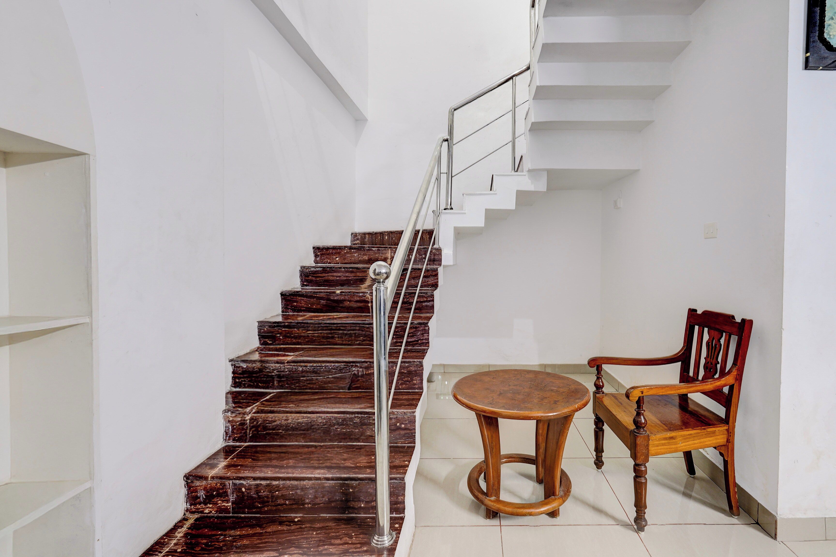 A staircase with wooden steps and a metal railing, leading to a landing with a wooden chair and a small round table.