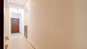 A corridor with a wooden door, a light switch, and a wall-mounted light fixture.
