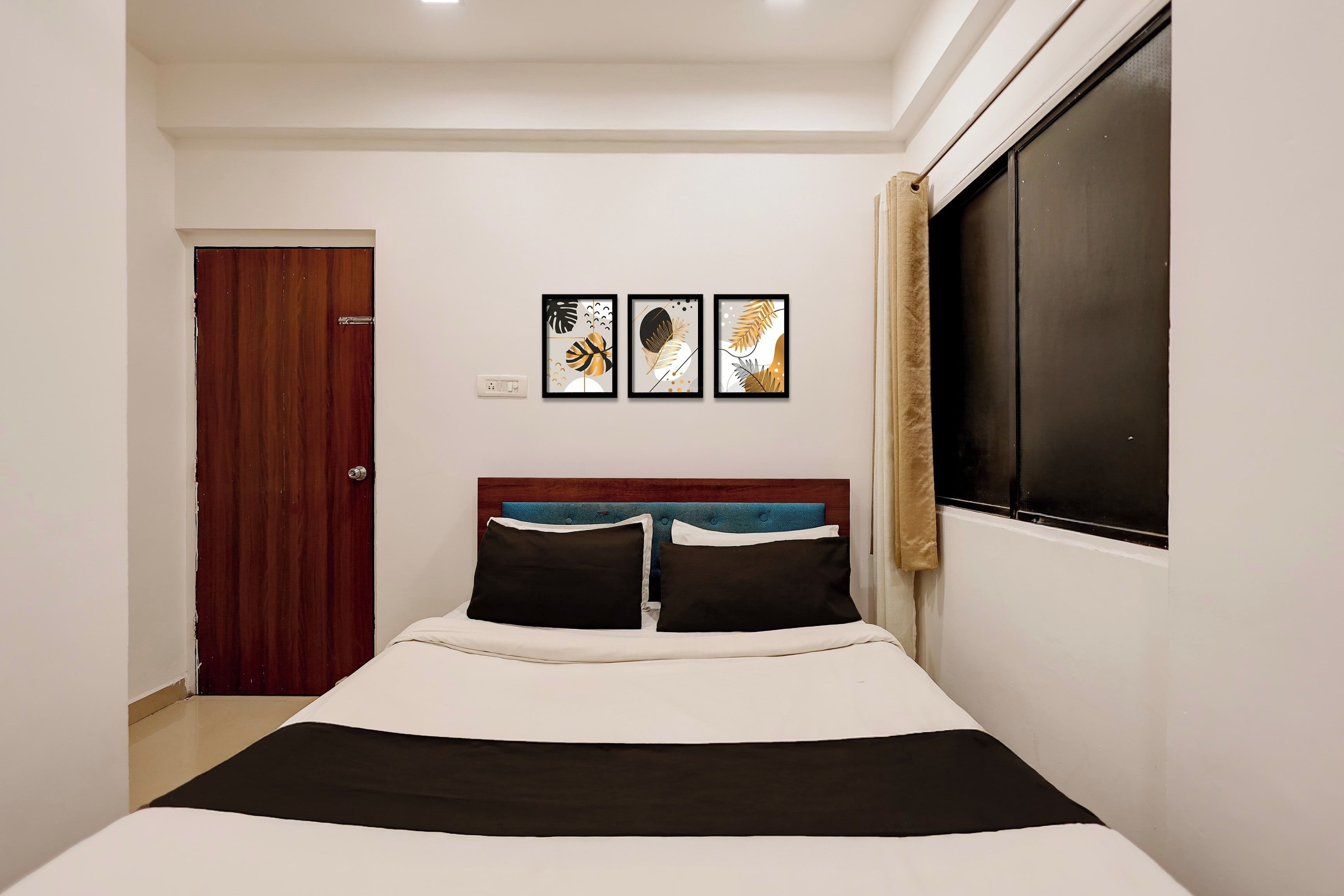 Un dormitorio con cama, ventana con cortinas, una puerta y tres cuadros en la pared.