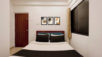 Un dormitorio con cama, ventana con cortinas, una puerta y tres cuadros en la pared.