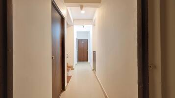 A narrow hallway with a wooden door on the left and a white wall on the right.