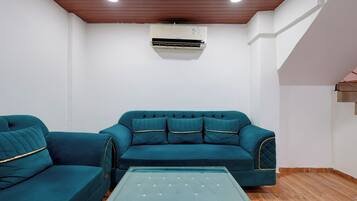 Una habitación con un sofá turquesa, una mesa de centro de vidrio y un equipo de aire acondicionado en la pared.