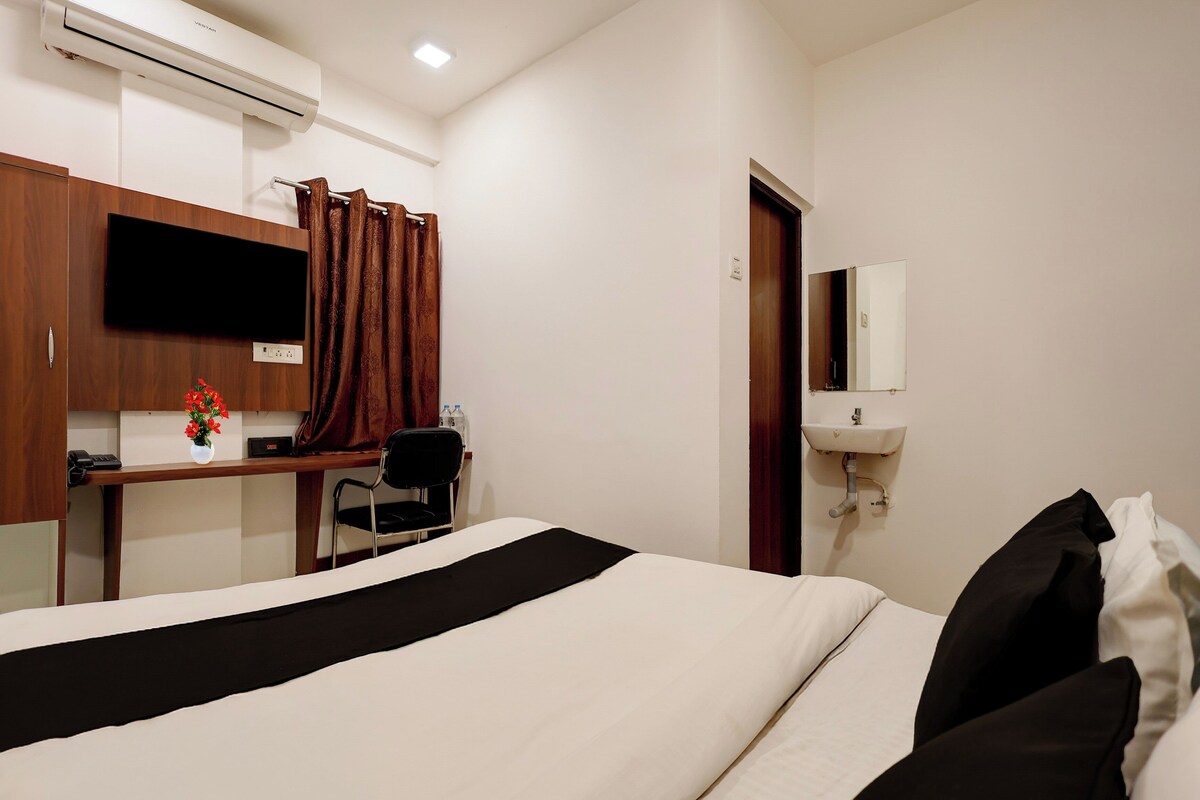 A hotel room with a bed, a desk with a chair, a television, a wardrobe, a bathroom with a sink, and a shower curtain.