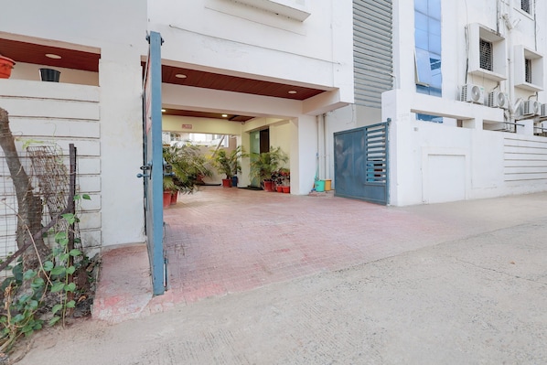 Uma entrada protegida por grades para um edifício, com um caminho de entrada pavimentado, vasos de plantas e um portão de metal.