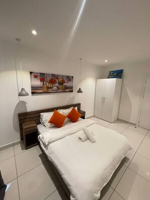 A bedroom with a bed, a nightstand, a wardrobe, a painting, and a ceiling light. - Luxury 3BR Apt w/ Pool, Gym Restaurant & DSTV - Embassy Gardens / 2 min from KIA (Accra)